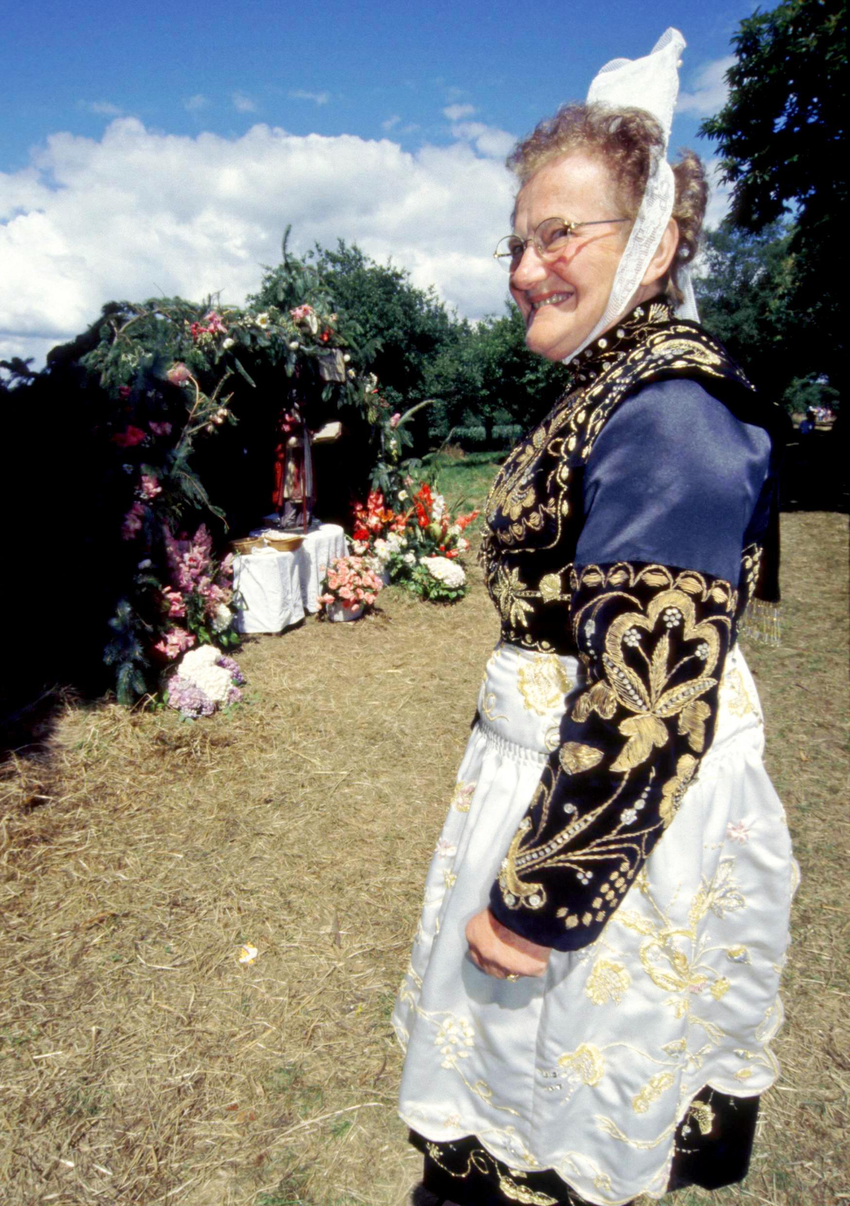 Eine Bretonin in Tracht steht neben einer der Laubhütten.