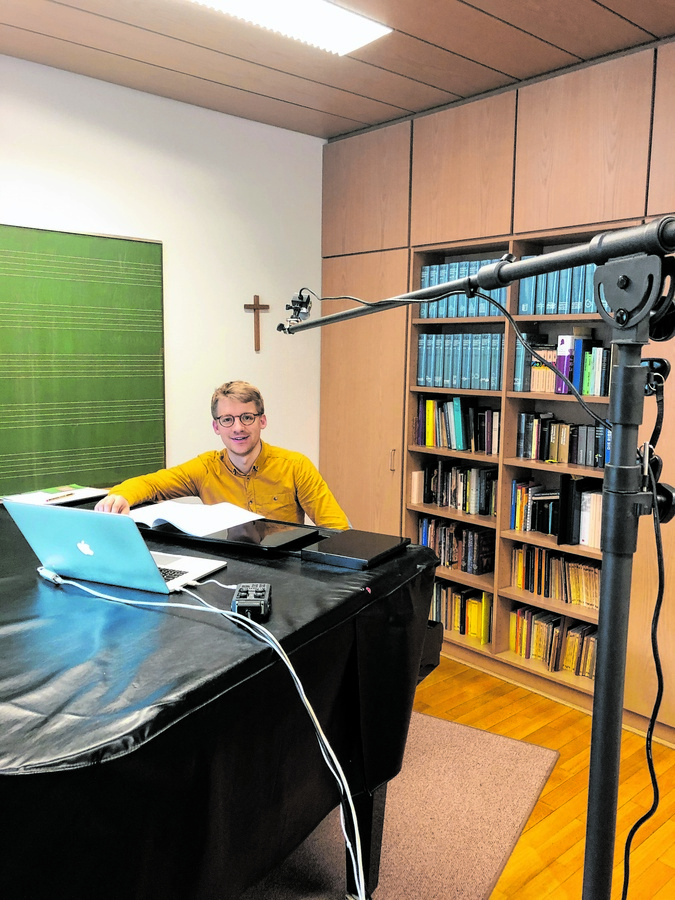 Domkapellmeister Stefan Steinemann sitzt mit Laptop und Mikrofon am Klavier. (Foto: Augsburger Domsingknaben)