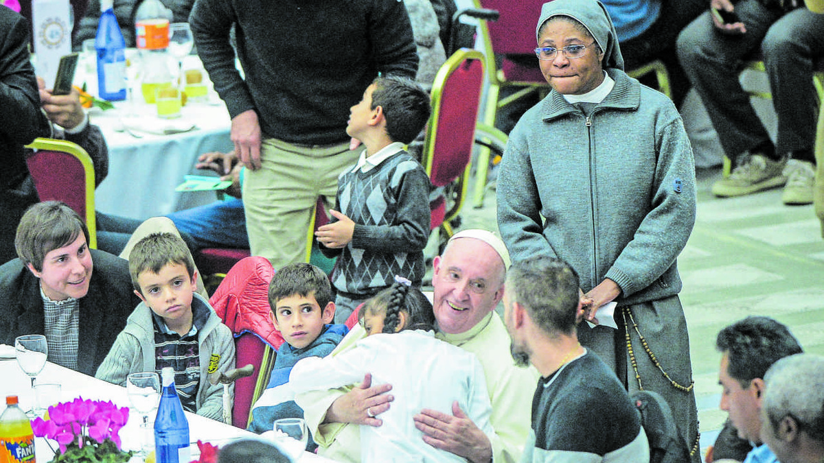 Während es sich ein kleines Mädchen bei ihm bequem gemacht hat, spricht Papst Franziskus mit anderen Gästen des gemeinsamen Mittagessens zum Welttag der Armen 2022 in der Audienzhalle.  (Foto: KNA)