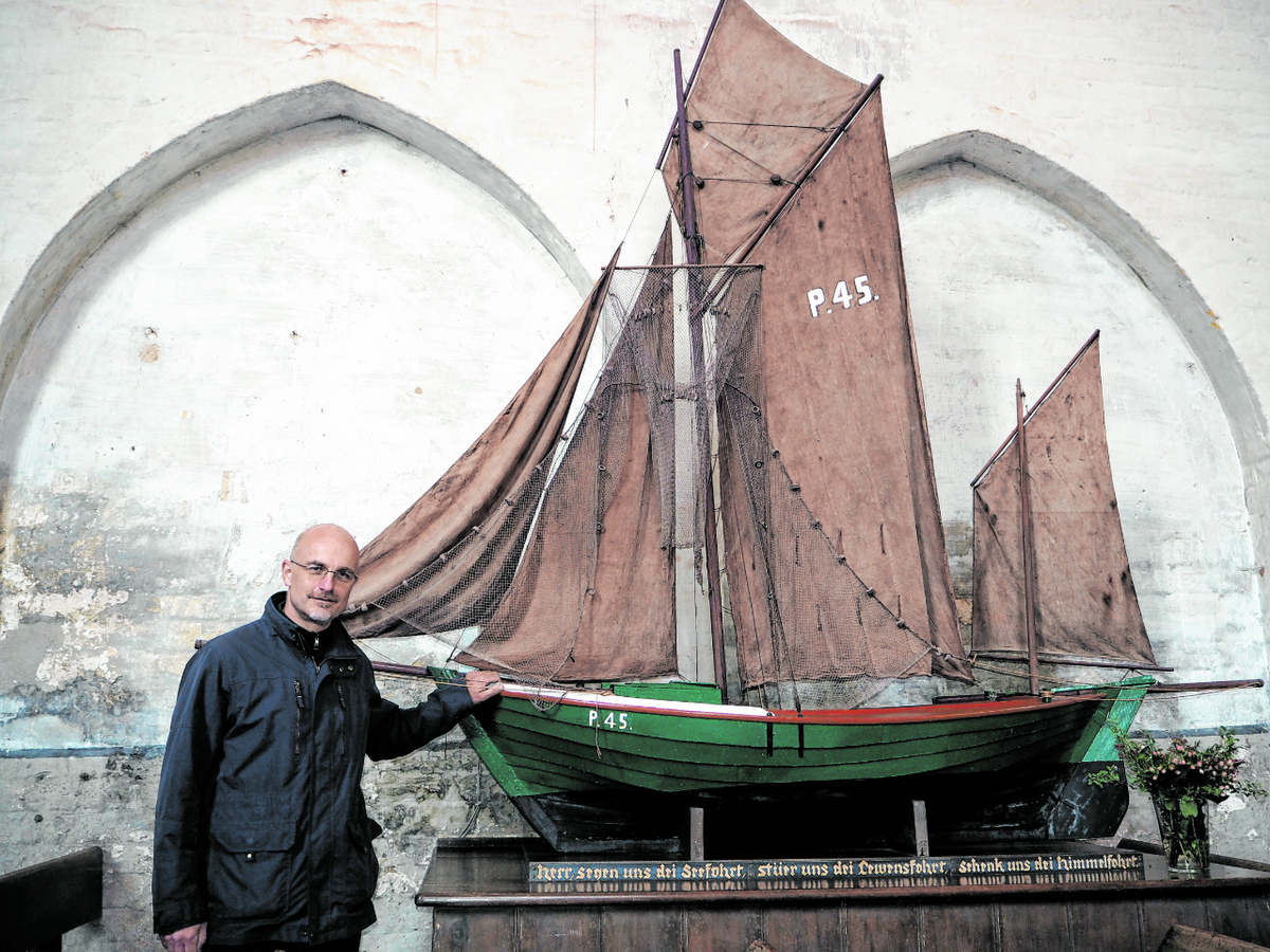 Pastor Johannes Staak vor dem nachgebauten Zeesboot – einem Schiff im Kirchenschiff. (Foto: Ludwig)