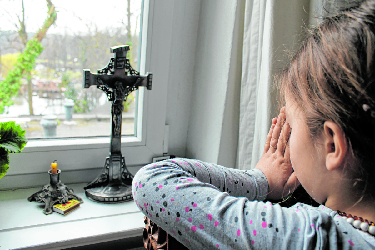 Wenn Gotteshäuser geschlossen sind und Gottesdienste ausfallen, ersetzt die Andacht zu Hause den Kirchgang. Die sechsjährige Lorenza, Schülerin einer katholischen Schule in Berlin, betet vor einem Kruzifix auf der Fensterbank. (Foto: Thiede)