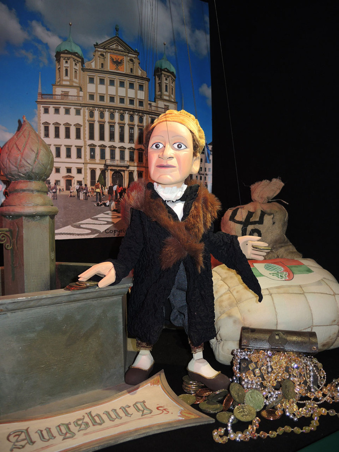 Jakob Fugger der Reiche lehnt sich an einen Brunnen. Im Hintergrund eine Abbildung des Augsburger Rathauses. (Foto: Mitulla)