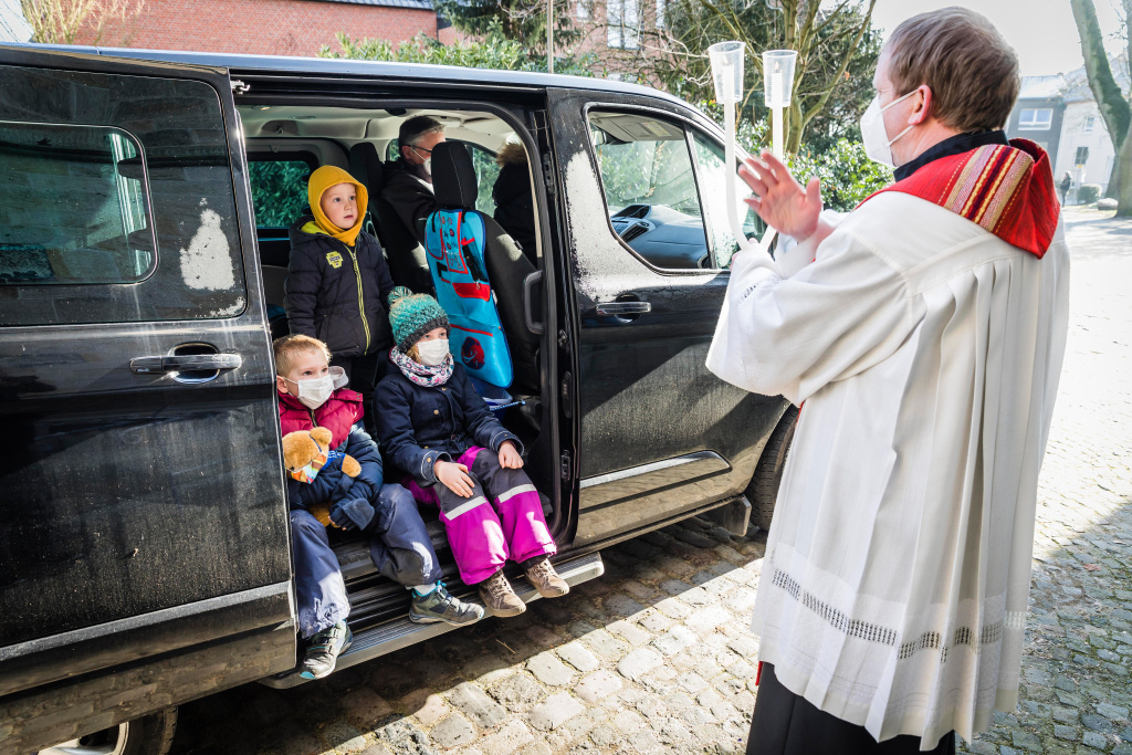 Pfarrer Markus Thoms hält zwei gekreuzte Kerzen und spendet vor dem Auto einer Familie den Blasiussegen im "Drive-in" am 31. Januar 2021 in Neuenkirchen. (Foto: KNA)