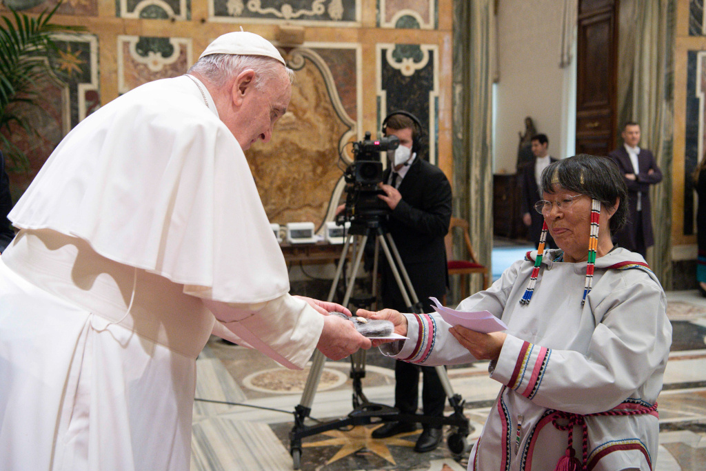 Papst Franziskus begrüßt Teilnehmer einer Delegation der indigenen Völker Kanadas am 1. April 2022 im Vatikan. Eine Frau überreicht dem Papst ein Geschenk. (Foto: KNA)