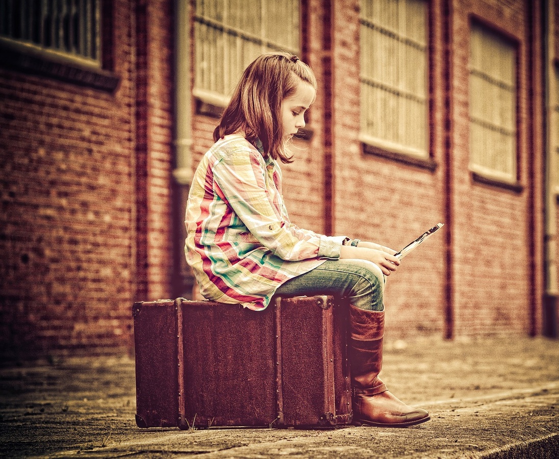 Ein Kind sitzt auf einem Koffer. (Symbolbild: gem)