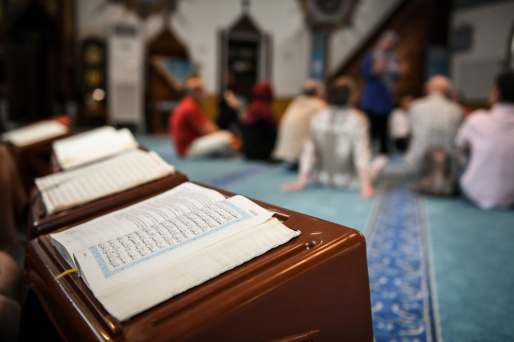 Koran-Bücher liegen aufgeschlagen auf kleinen Bänken in einer Moschee in Heidelberg. Besucher sitzen während einer Moschee-Führung auf dem Gebetsteppich. (Foto: KNA)