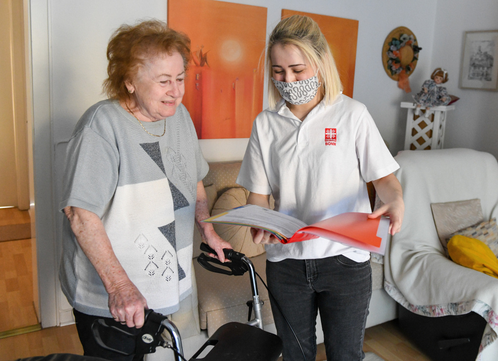 Eine Mitarbeitern der Ambulanten Pflege der Caritas trägt Mundschutz und spricht mit einer Patientin in deren Wohnung in Bonn am 22. April 2020. (Foto: KNA)