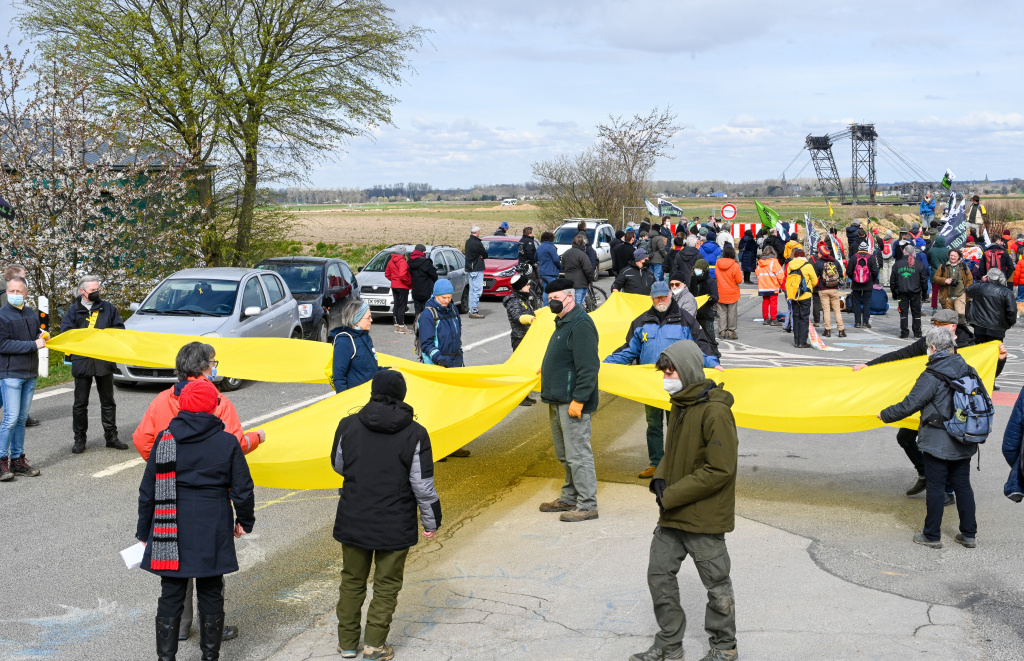Demonstranten der Initiative "Kirche(n) im Dorf lassen" tragen ein Kreuz aus gelbem Stoff zum Grenzwall an der Grube des Tagebaus Garzweiler II. im Ortsteil Lützerath in Erkelenz am 3. April 2022. (Foto: KNA)